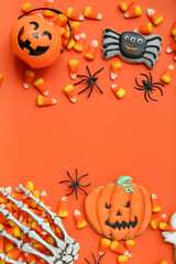 Tasty Halloween candy corns, skeleton hand and cookies on orange background