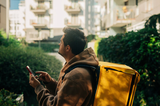 Food delivery person with yellow backpack searching address on smart phone