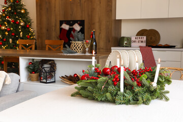 Christmas wreath with burning candles on white table in kitchen