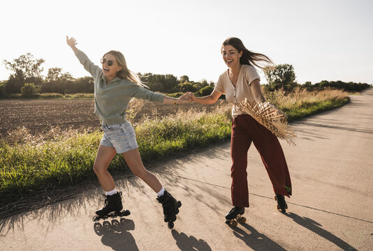 Cheerful young friends roller skating on road near field
