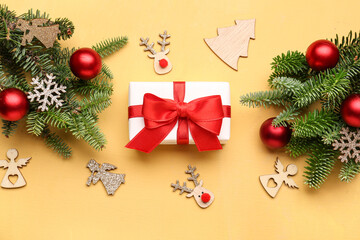 Christmas tree branches with decorations and gift box on yellow background