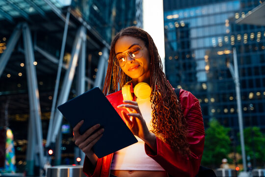 Smiling woman with headphones and long braided hair using tablet PC - Powered by Adobe