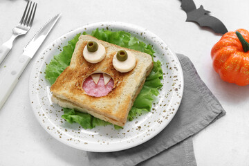 Plate with funny Halloween sandwich, cutlery and decorations on light background, closeup