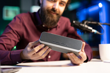 Close up shot of mini soundbar presented by cheerful online star doing technology reviews. Focus on high end music playing device presented by influencer in blurry background