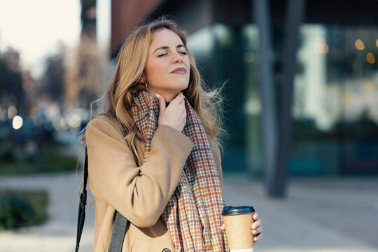 Blond woman touching neck and holding disposable cup