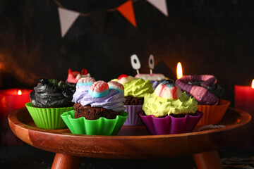 Wooden stand with delicious Halloween cupcakes on dark background, closeup