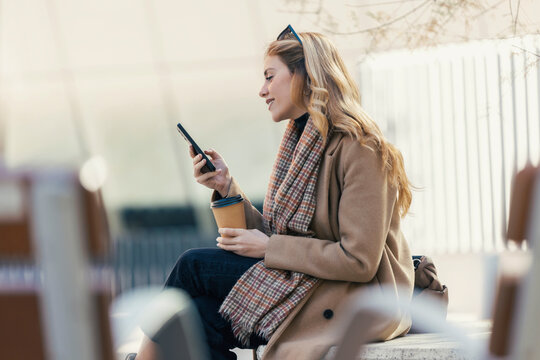 Blond woman spending leisure time using smart phone on city