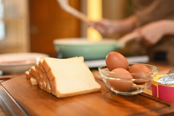 Sliced bread arranging on a wooden cutting board next to a glass bowl filled with brown eggs
