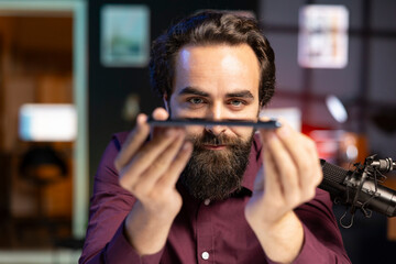 Tech guru reviewing latest phone, impressed by its thinness while filming technology internet show...