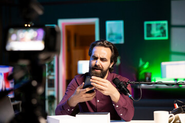 Tech specialist assessing cellphone performance, confused about subpar components used, filming with professional camera and mic. Entertainer shooting phone review, puzzled about inside parts used