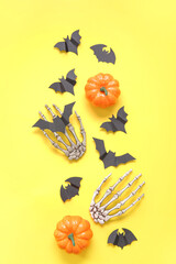 Composition with pumpkins, paper bats and skeleton hands on yellow background. Halloween celebration concept