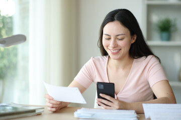 Happy asian woman holding bill paying with phone at home