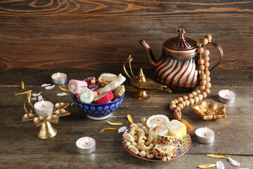 Diya lamps with candles, beads, teapot and plates of different treats on brown wooden background. Divaly celebration