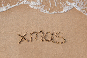 Xmas written on sandy beach sea. Top view. Flat lay.