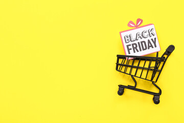 Greeting card with text BLACK FRIDAY in shopping cart on yellow background