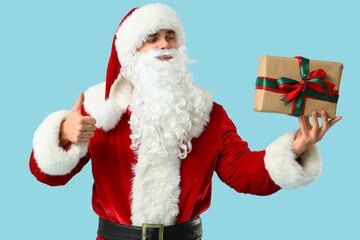 Santa Claus with gift box showing thumb-up gesture on blue background