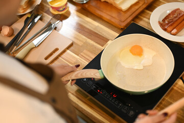 Cropped shot of young woman cooking an egg in a frying pan on electric stovetop
