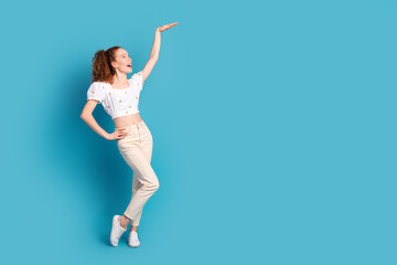 Full size photo of pretty young girl show high measure empty space wear trendy white outfit isolated on blue color background