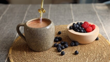 Creamy orange smoothie in rustic gray mug paired with vibrant berries in wooden bowl on woven surface highlights balanced eco-friendly snack focused on clean eating and wellness.