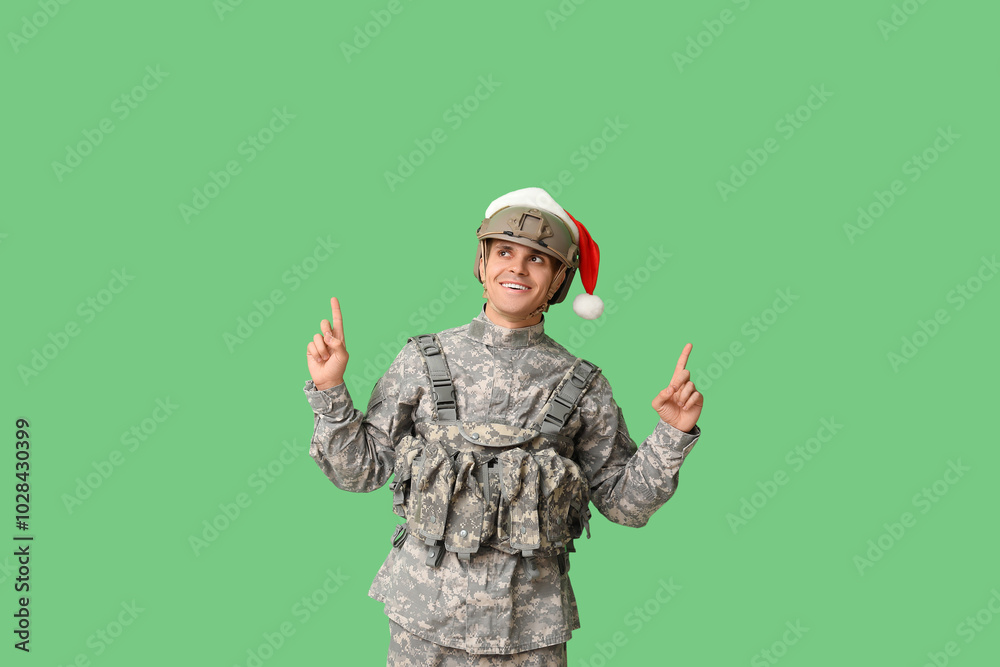 Wall mural Male soldier with Santa hat pointing at something on green background