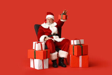 Santa Claus with many gift boxes sitting on armchair against red background