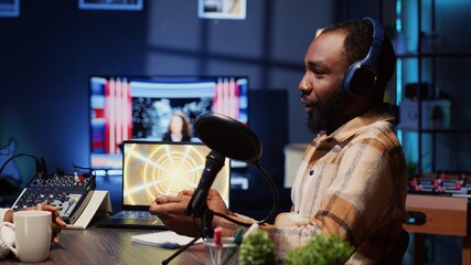 Online show host speaking with guest during live broadcast for social media platforms, listening to her opinion. African american influencer using professional gear to record podcast