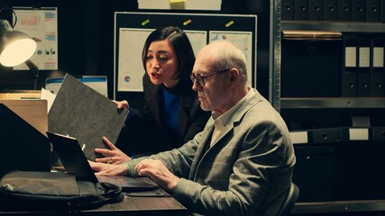Private detectives reviewing forensic evidence folders in police archive room, collaborating on...