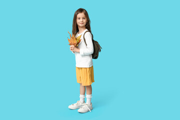 Cute little girl in stylish clothes with backpack and autumn leaves on blue background