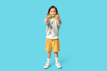 Cute little girl in stylish clothes with pumpkins on blue background