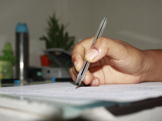 Close-Up of a woman is writing on a piece of paper with a pen with Blurred Background