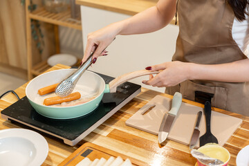 Asian woman grilling sausages and bacon for breakfast
