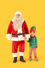 Santa Claus and cute little elf holding hands on yellow background