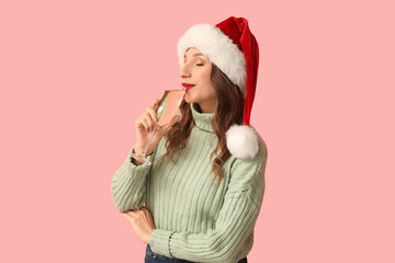 Young woman in Santa hat with glass of champagne on pink background