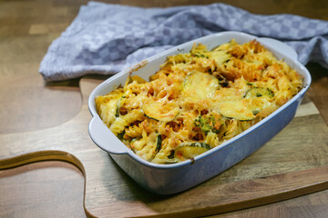 Baked pasta with cheese and vegetables in a blue casserole with a kitchen towel on a rustic wooden board, homemade meal, selected focus