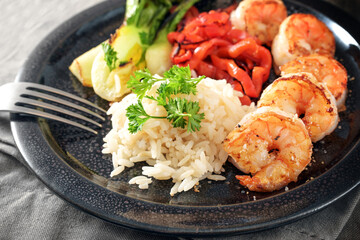 Fried prawns or shrimps with rice and vegetables on a dark plate, homemade Asian style meal, copy space, selected focus