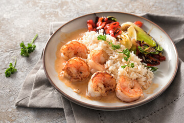 Fried prawns with crustacean sauce, rice and vegetables on a gray plate and beige napkin on a stone background, cooking a healthy homemade dish, copy space, selected focus
