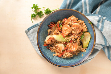 Shrimps or prawns with rice and vegetables on a blue plate and a kitchen towel on a light wooden background, healthy cooking at home, top view from above, selected focus