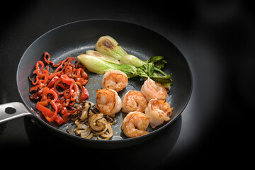 Fried prawns and vegetables such as bok choy, red bell peppers and onions in a frying pan on a black induction stove, cooking a healthy meal for low carb diet, copy space