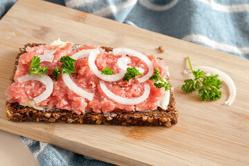 Mett with onions and parsley on a slice of dark wholemeal bread on a kitchen board, German specialty from minced raw pork with low fat seasoned with salt and black pepper, copy space
