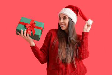 Young woman in Santa hat with Christmas gift box on red background