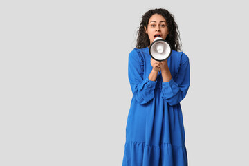 Surprised African-American woman with megaphone on light background