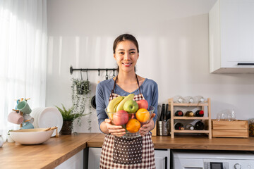 Portrait of Asian young woman hold a bowl of fruits and look at camera. 
