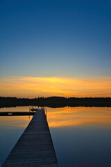 Obraz premium Wooden jetty at sunset on a Swedish lake. The colors are reflected in the water