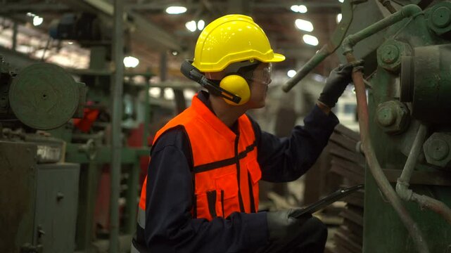 Professional technician man with safety helmet analyzing and maintenance with tablet in factory warehouse. Asian technician factory inspection and control machine in industry factory.