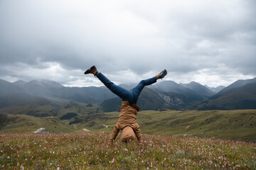 Woman hiker doing a handstand on high altitude mountain top grassland
