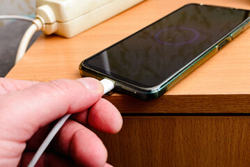 Mans hand plugging a charger in a smart phone at home.