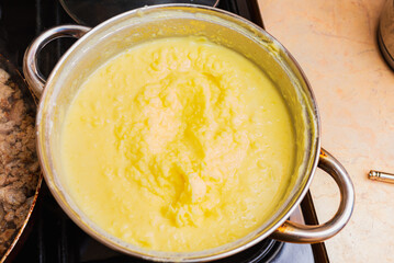 Mashed potatoes in an enamel pot are prepared on the stove.