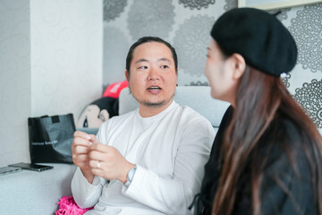 A Korean man and a Japanese woman, both in their 30s, are sitting on a sofa and talking in an...