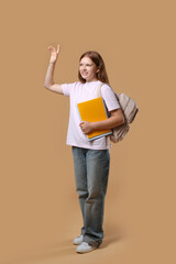 Teenage girl with backpack and books on beige background