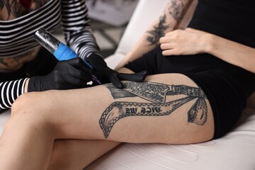 Professional artist tattooing woman's leg with machine in salon, closeup